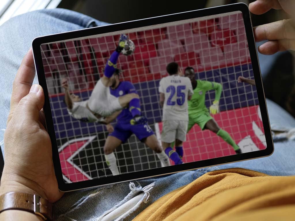 Eine Hand hält ein Tablet, auf dem ein Fußballspiel läuft.