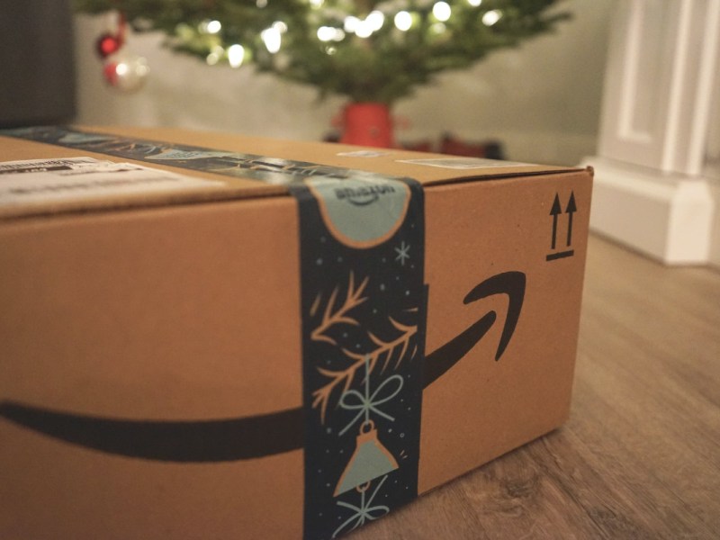 Paket von Amazon liegt auf Holzboden vor geschmücktem Tannenbaum