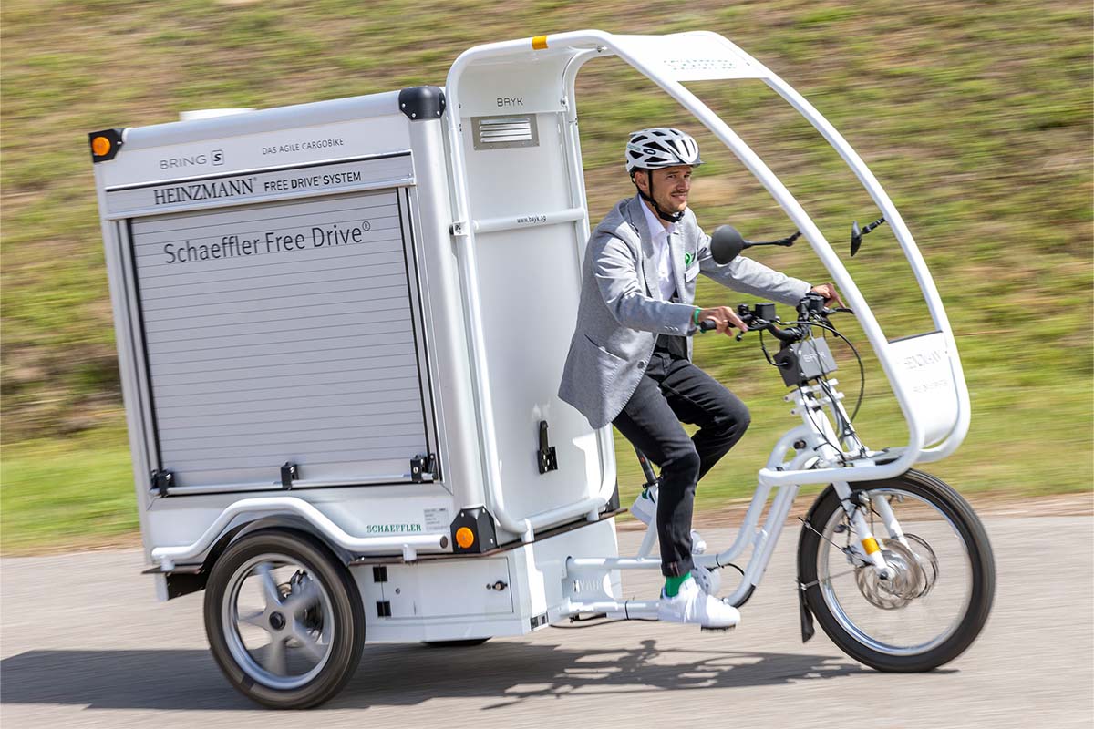 E-Cargo-Bike mit großer Ladebox im Heck und Regenschutz für den Fahrer, Mann fährt auf diesem Bike