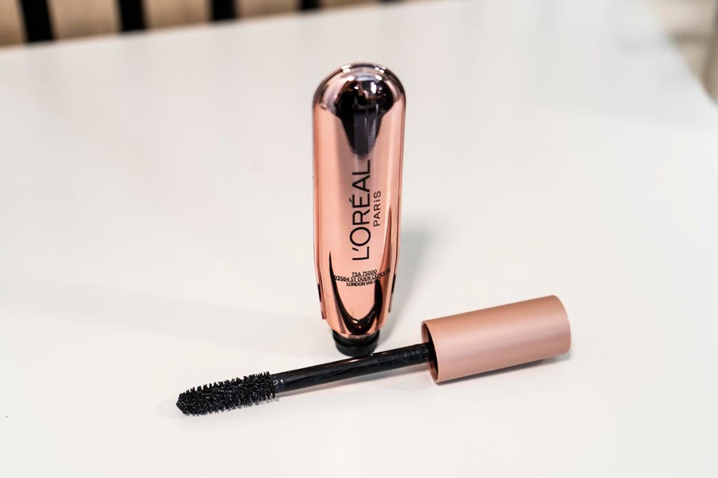 Bronze farbene Mascara geöffnet mit Bürste davor auf weißem Tisch