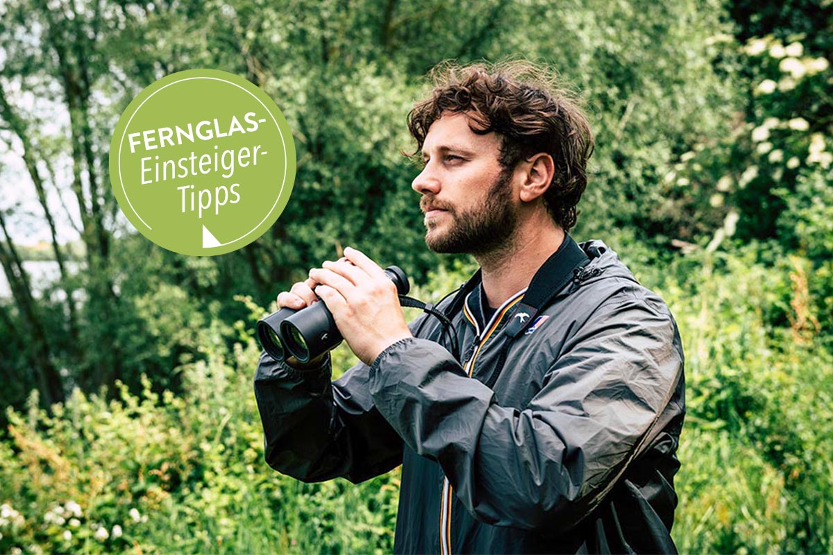 Mann mit Fernglas in der Hand in einem Wald.