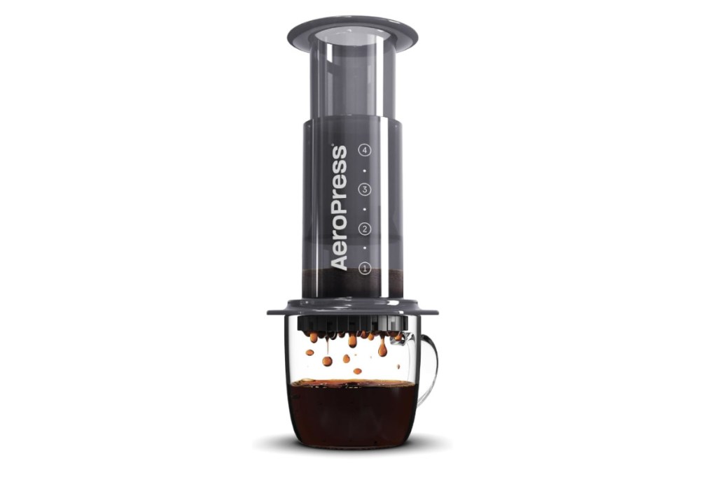 Dunkle zylinderförmige Aeropress auf Glassbecher in den Kaffee tropft auf weißem Hintergrund