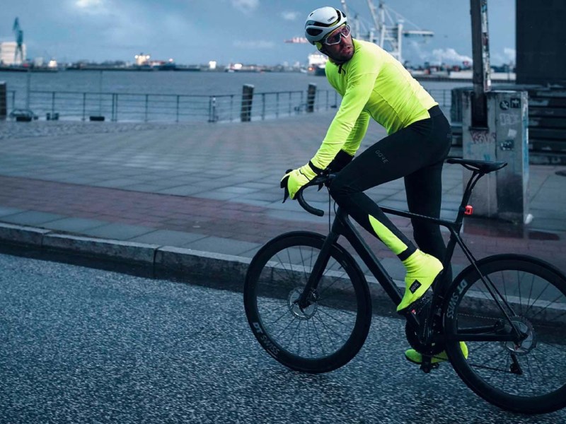 Gravelbikefahrer in der Dämmerung, trägt grelle Kleidung und Überschuhe