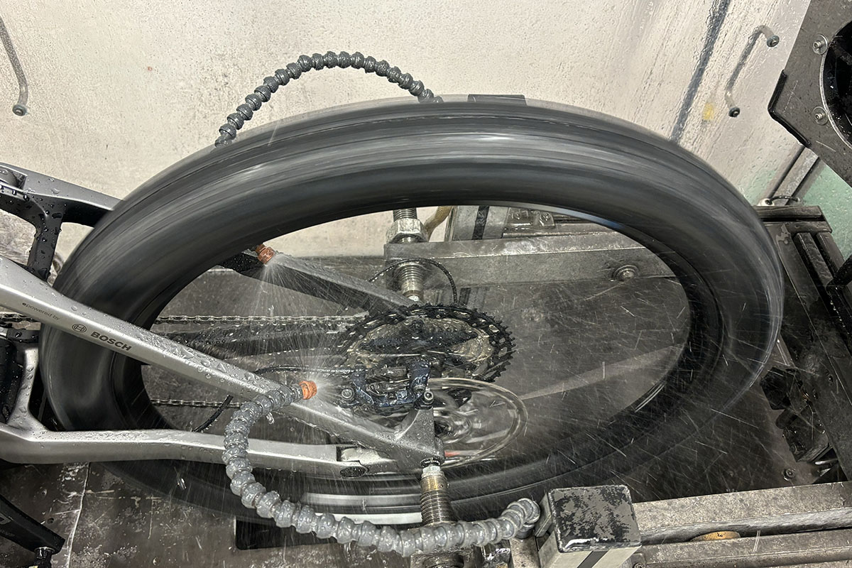 Detailaufnahme von einem Hinterrad eines E-Bikes das in einem Bremsenteststand begfestigt ist. Für die Prüfung der Scheibenbremsen im feuchten Zusatnd wird Wasser auf die Scheibenbremsen gesprüht.