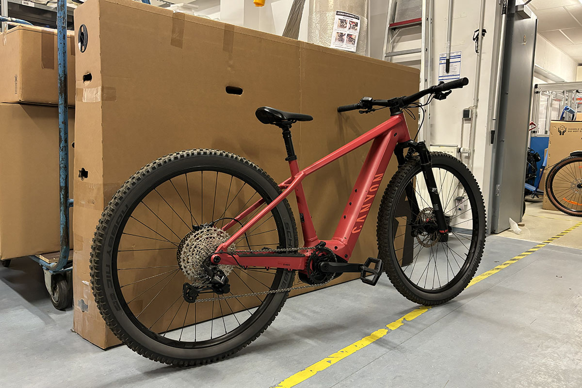Rotes E-Bike im Profil steht vor einem Karton in Lagerhalle.