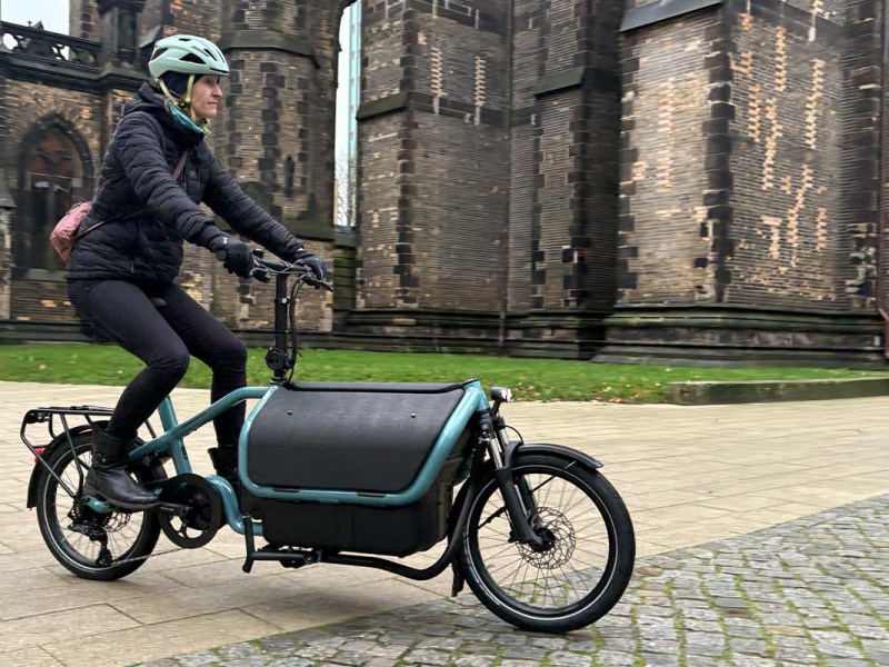 Frau fährt mit einem Cargo-E-bike vor einer Kirche lang