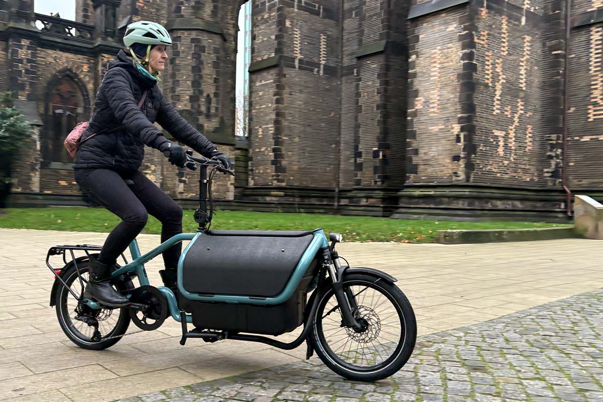 Frau fährt mit einem Cargo-E-bike vor einer Kirche lang