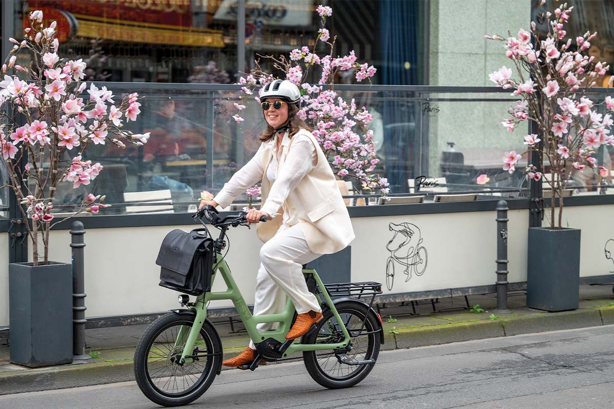 Frau fährt mit einem kompakten E-bike eine Straße entlang, dahinter blühende Bäume