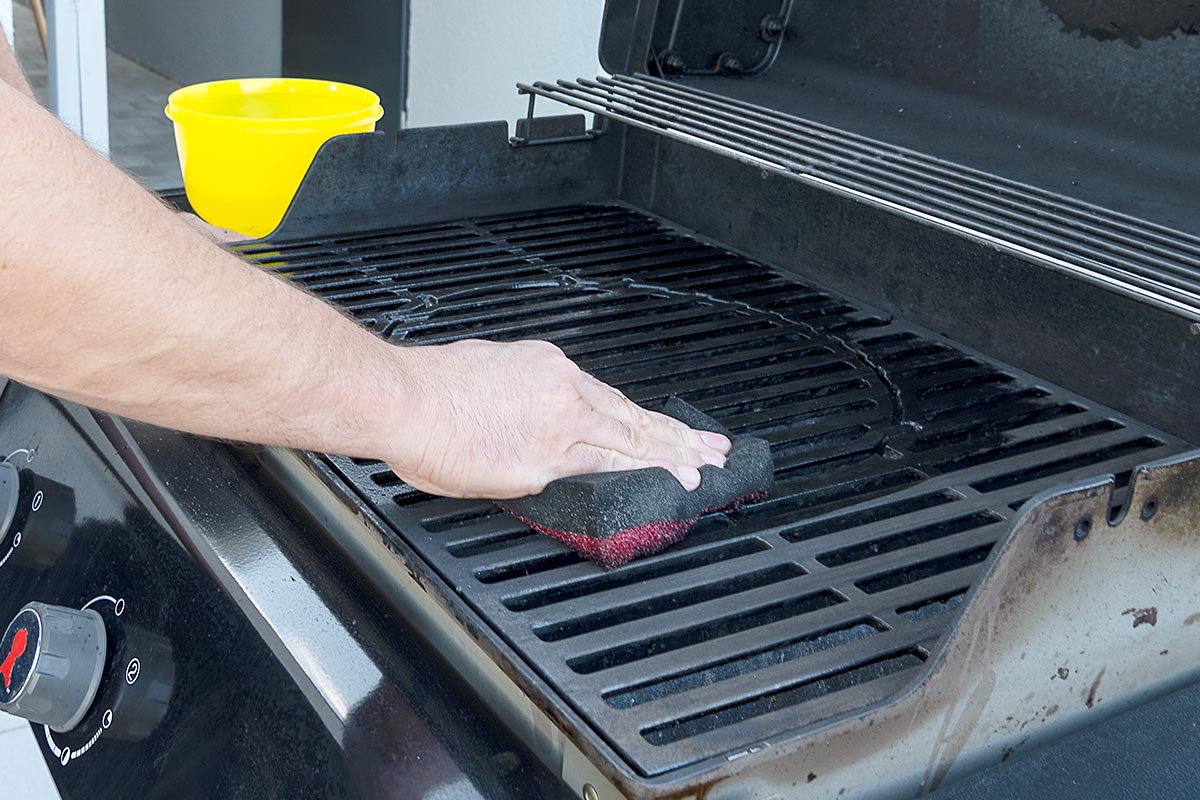 Person reinigt mit einem Schwamm einen Gasgrill.