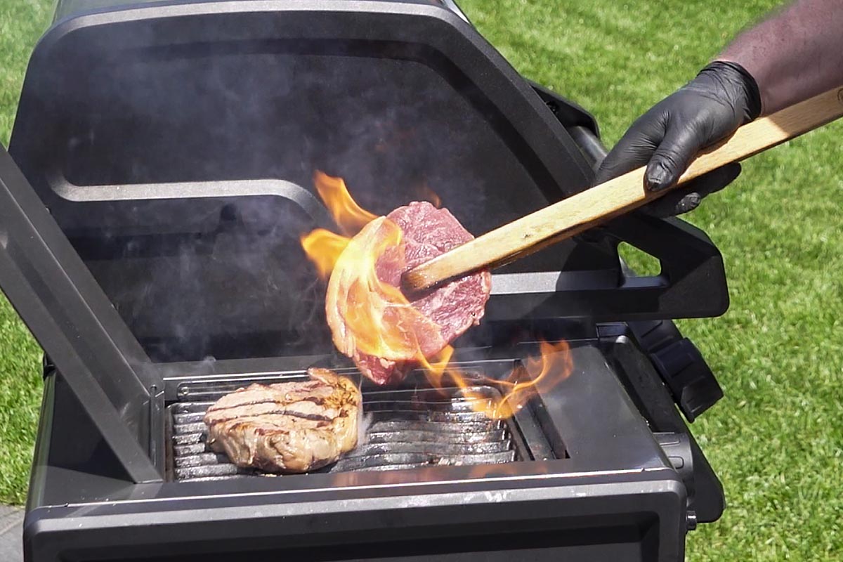 Person wendet ein StÃ¼ck Fleisch auf einem Grill.