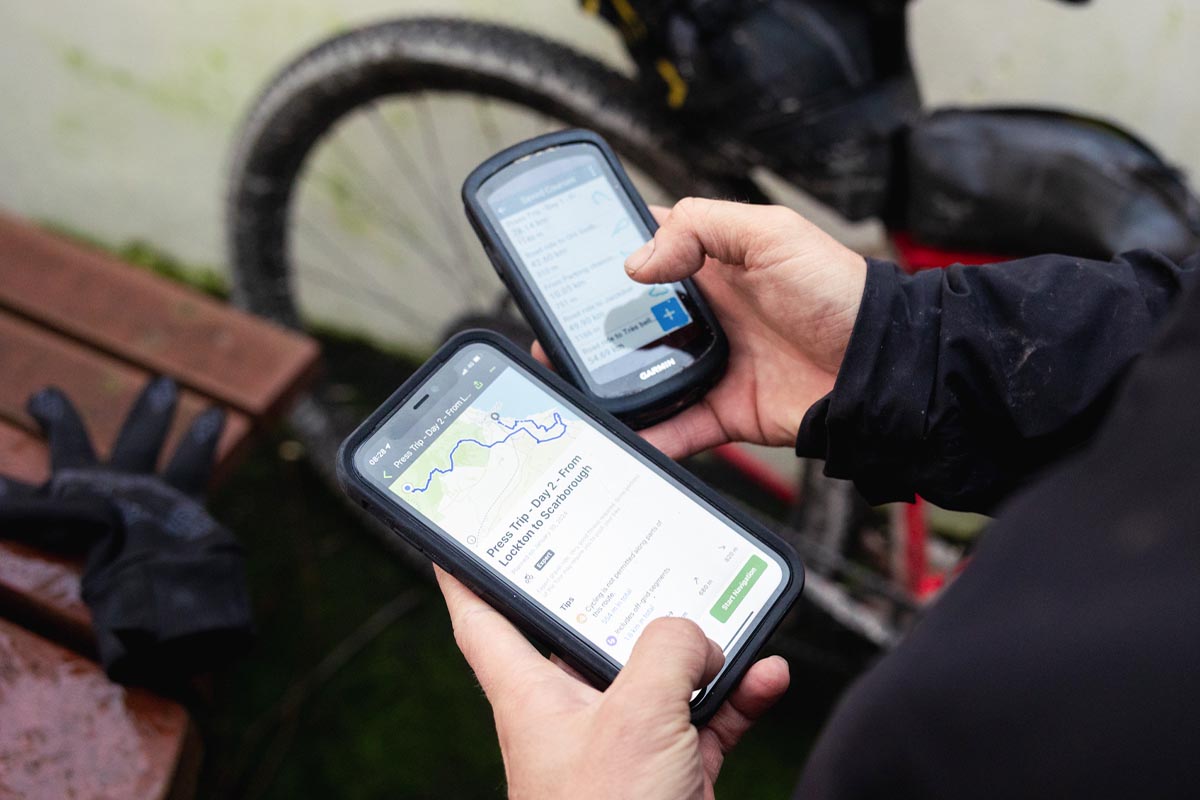 Person hält Smartphone und Navigationsgerät in der Hand.