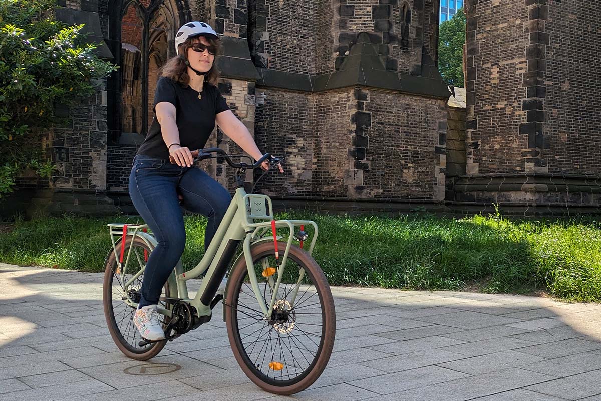 Frau fährt mit einem Fahrrad über einen Platz, Kirche im Hintergrund