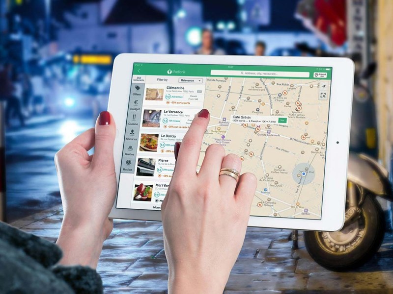 Blick auf ein Tablet, man sieht Google Maps, ein Finger tippt auf der Karte