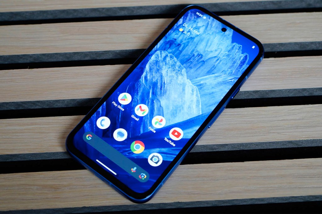 Das eingeschaltetet Google Pixel 8a liegt auf einer Holzoberfläche.