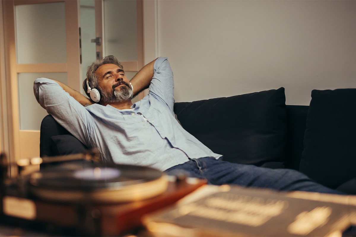 Ein Mann sitzt entspannt auf einem Sofa und trägt Kopfhörer.
