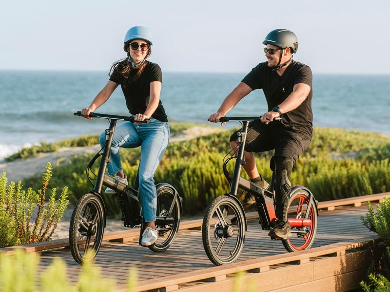 Zwei Personen mit Helm fahren auf einem E-Bike.