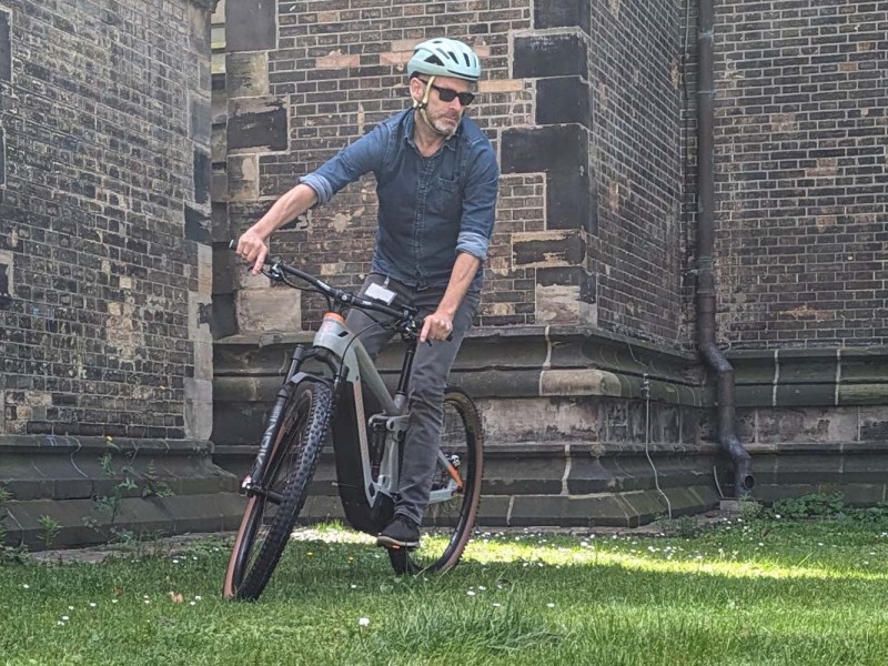 Mann fährt auf einem E-Mountainbike, Kirche im Hintergrund