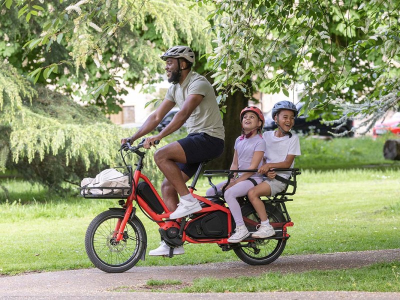 Mann auf einem kompakten E-Lastenrad, zwei Kinder auf dem Rücksitz