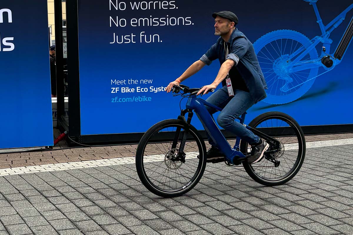 Mann fährt mit einem E-Bike, hinter ihm ein blaues Werbeplakat