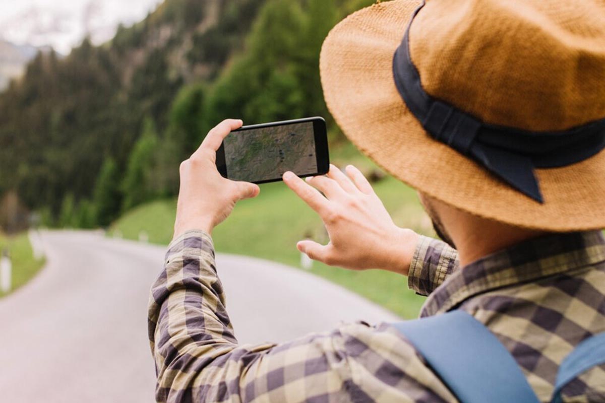 Person hält ein Smartphone in der Hand und steht auf Asphalt.