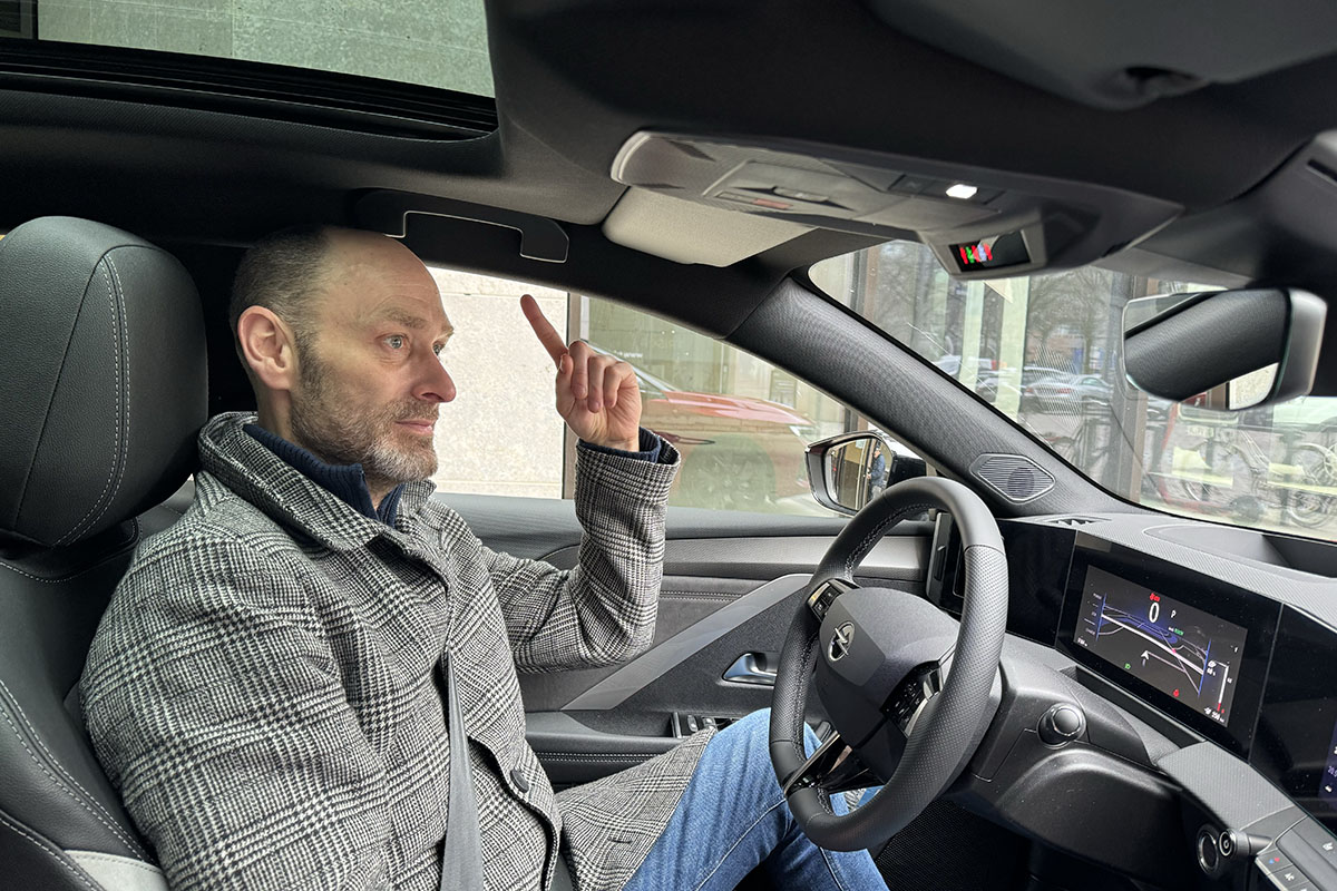 Mann sitzt im Cockpit des E-Autos Opel Astra Sports Tourer Electric und zeigt auf das Dach über seinem Kopf.