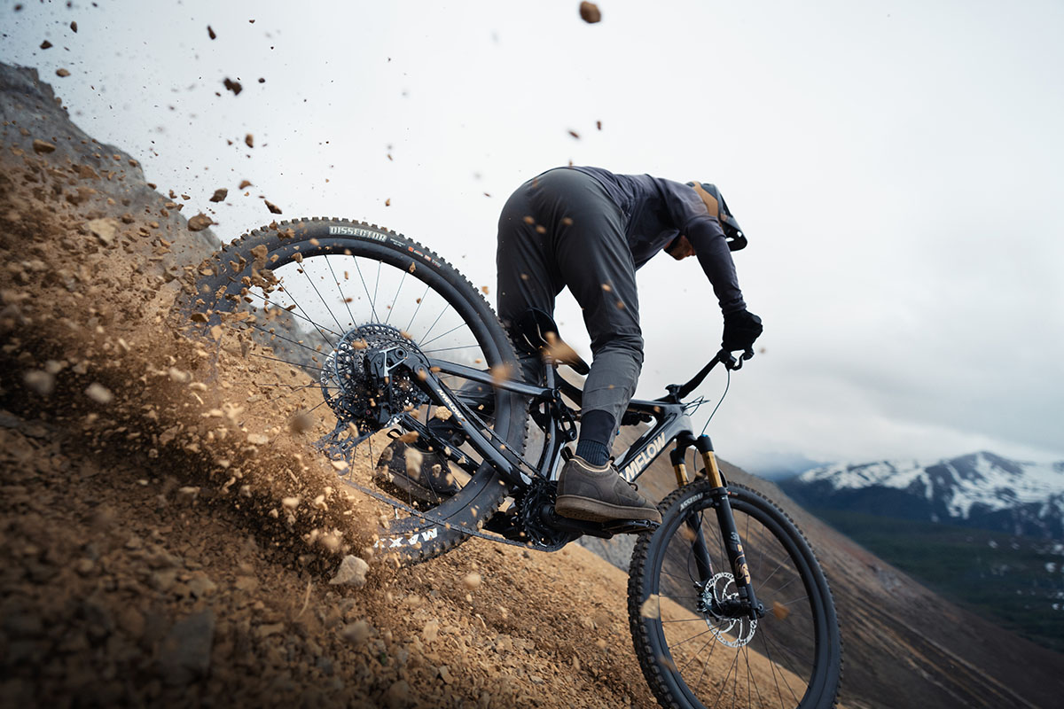 Mann fährt rasant bergab mit einem E-Mountainbike, so dass Sand und Steine herumwirbeln.