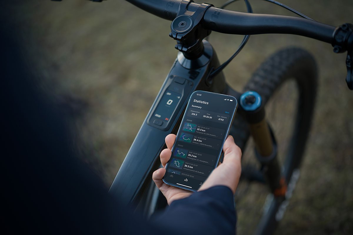 Detailaufnahme die zeigt, wie eine Hand ein Smartphone hält, über das Einstellungen für E-Mountainbike vorgenommen werden können.