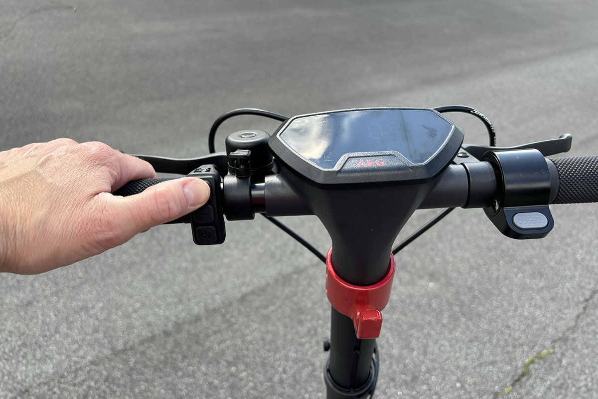 Detailaufnahme eines Lenkers bei einem E-Scooter mit Display und Bedienmodulen für die Wahl der Unterstützungsstufen. Eine Hand hält dabei einen Lenkergriff.