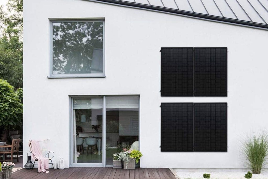 Solarpanels an der Fassade eines weißen Hauses mit Terrasse.