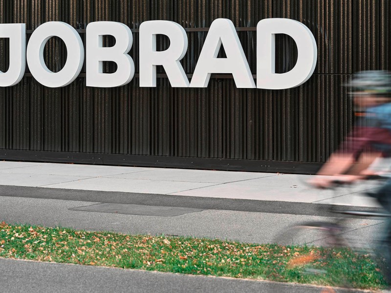 Ein großes JobRad-Logo hängt als Schild an einer Holdwand. Im Vordergrund fährt ein Radfahrer auf einem Fahrradweg.