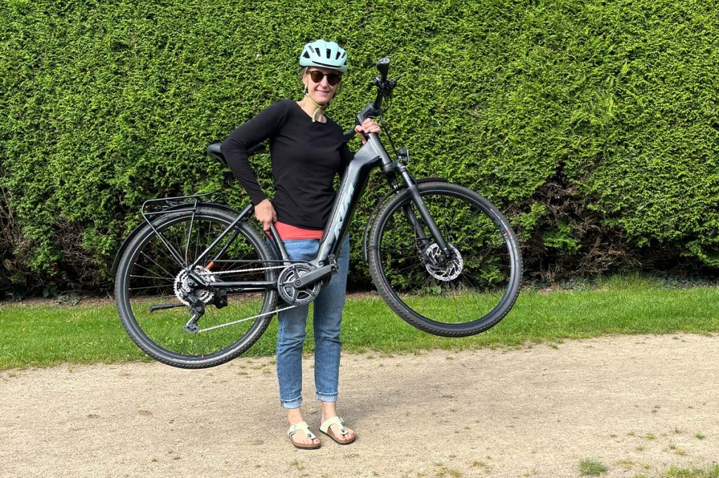 Frau steht in einem Park und hebt ein E-Bike hoch