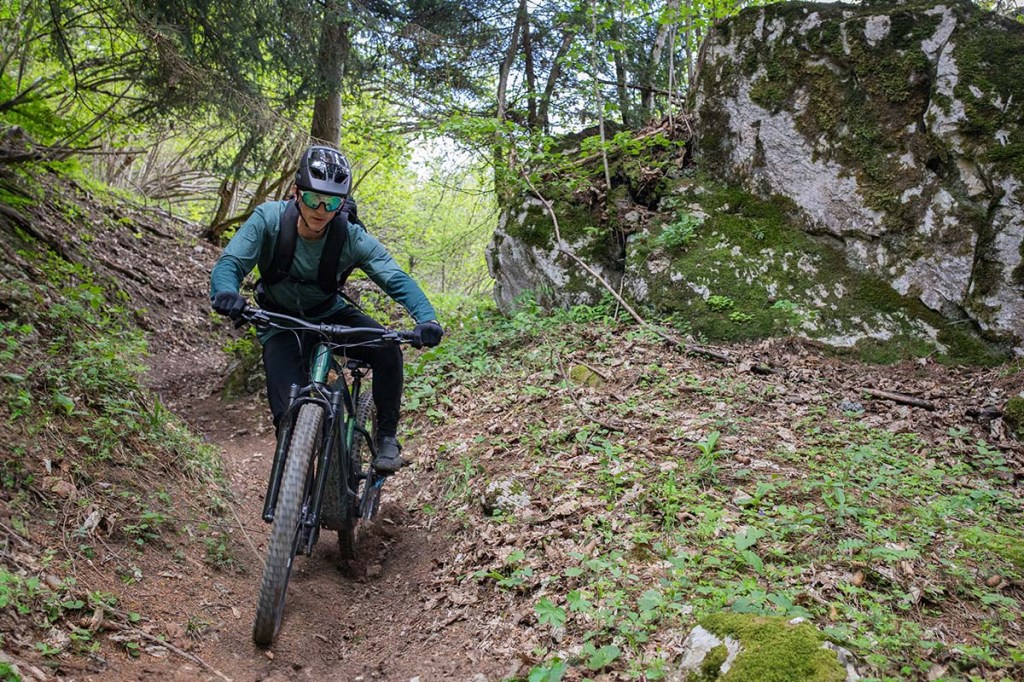 Mann fährt mit einem E-Mountainbike einen steilen Trail im Wald herunter