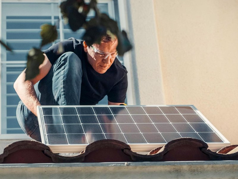 Person befestigt ein Solarmodul auf einem Dach.