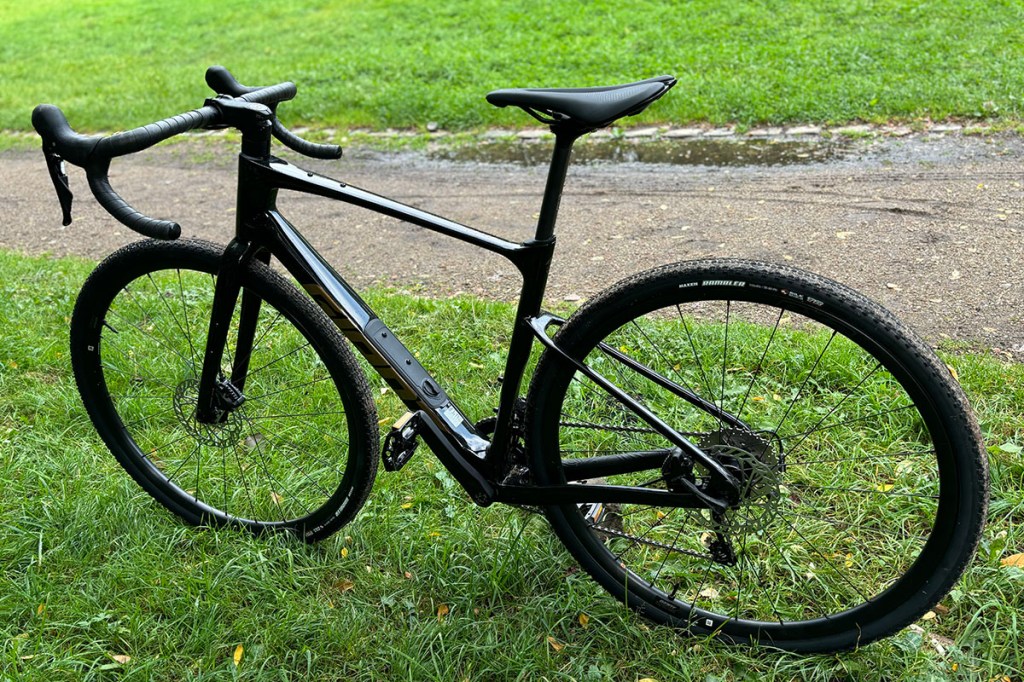 Schwarzes Gravelbike steht im Profil vor einer Weise.