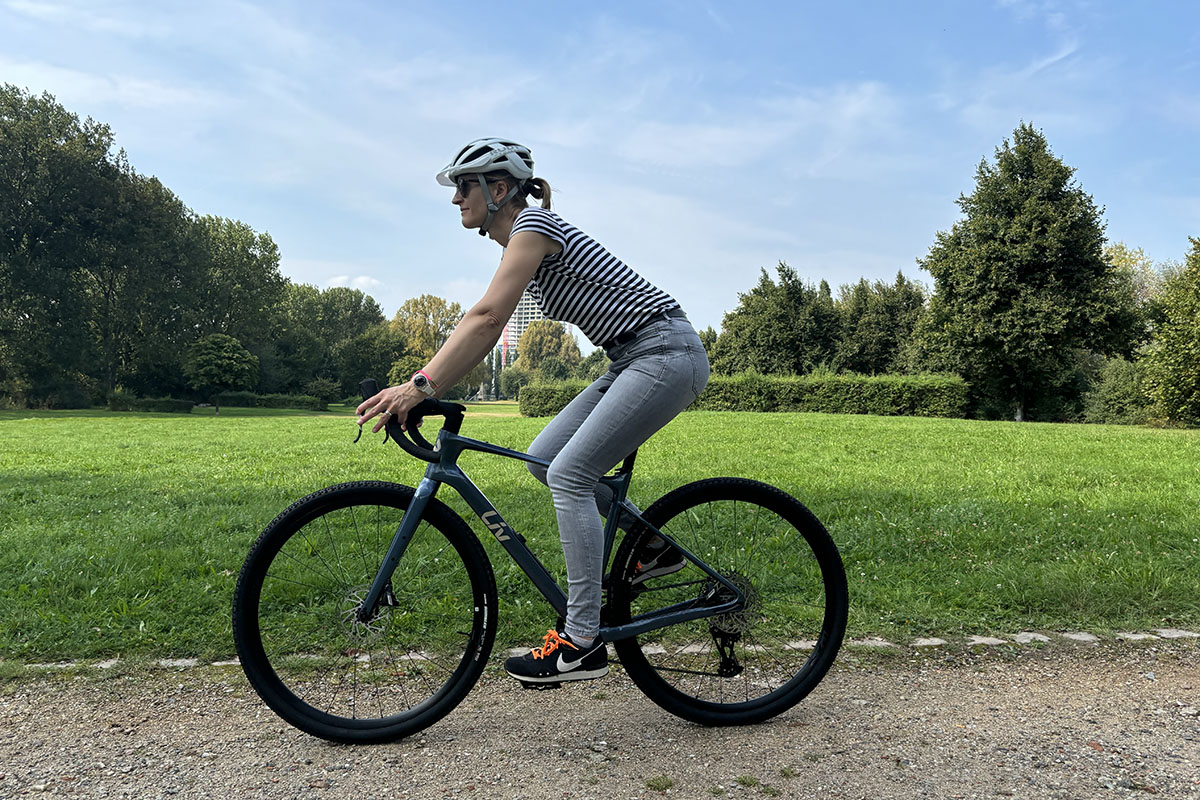 Frau fährt auf einem Gravcelbike durch eine Parklandschaft.