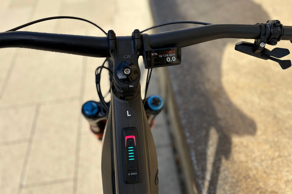 Detailansicht eine E-Bike-Lenkers mit kleinem Fahrdisplay, das rechts von der Lenkerstange angebracht ist.