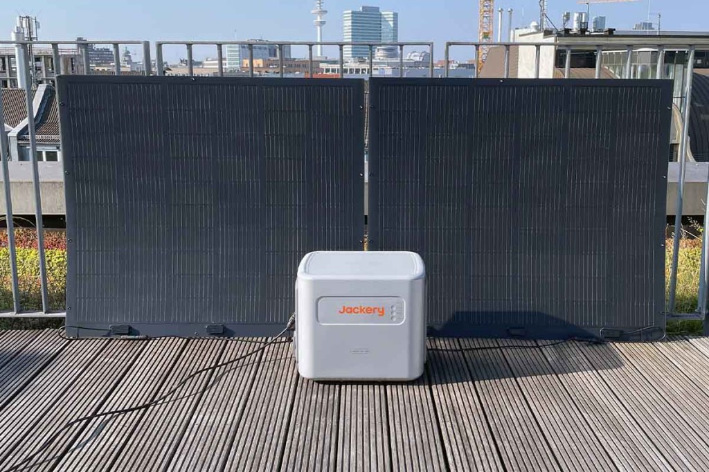 Der Navi 2000 Speicher von Jackery auf Holzplanken mit Solarpanels im Hintergrund.