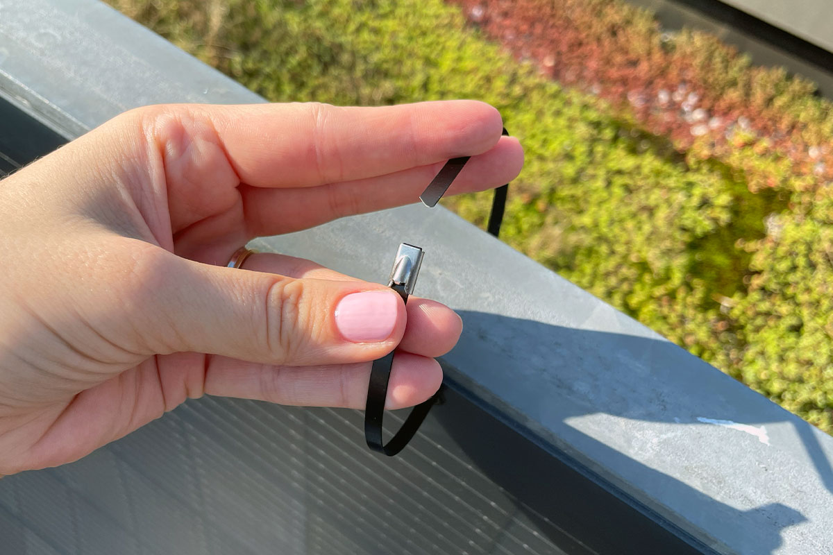 Eine Person befestigt ein Jackery-Panel mit einem Kabelbinder am Balkongeländer.