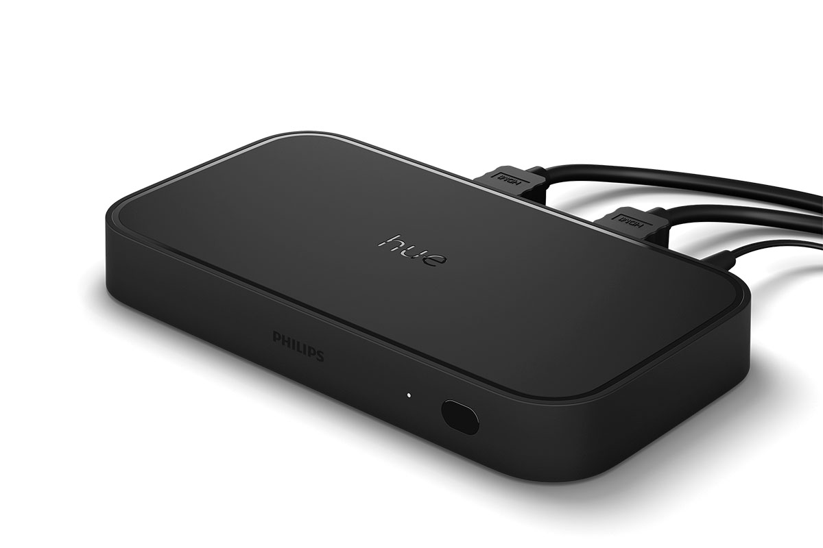 Philips Hue Play HDMI Sync Box 8K in schräger Ansicht mit eingesteckten HDMI-Kabeln vor weißem Hintergrund.