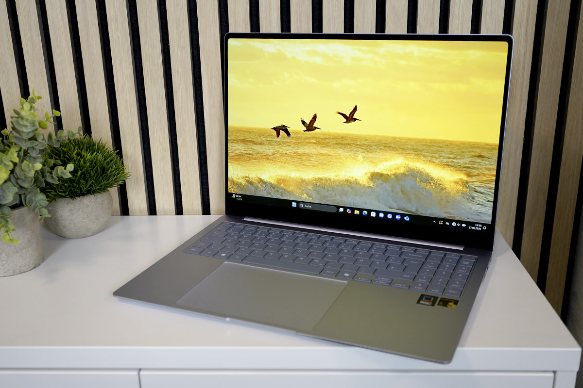 Das Notebook Samsung Galaxy Book 4 Edge steht eingeschaltet auf eine hellen Sideboard vor einer holzverkleideten Wand