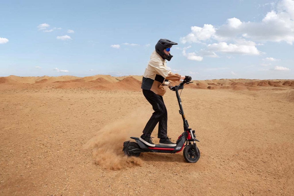 Person auf einem E-Scooter, fährt auf einem Schotteruntergrund