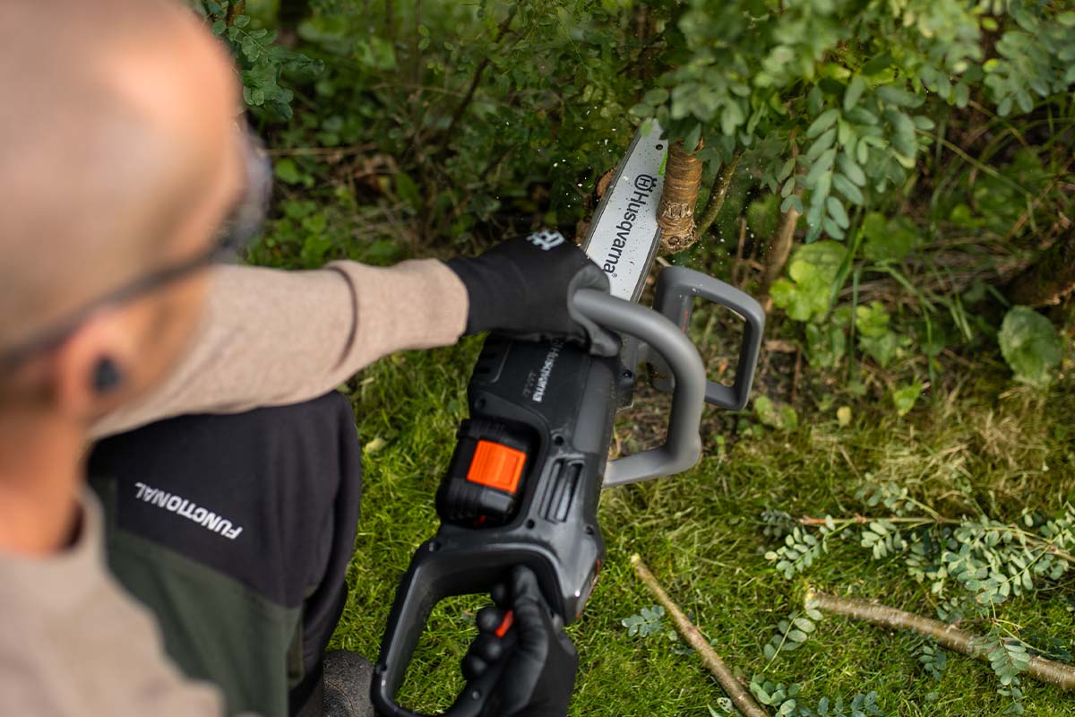 Overshoulder-Blick einer Person mit einer Kettensäge, die einen Ast durchsägt