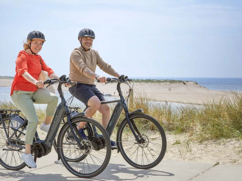 zwei Personen fahren mit dem E-Bike an einem Strand entlang