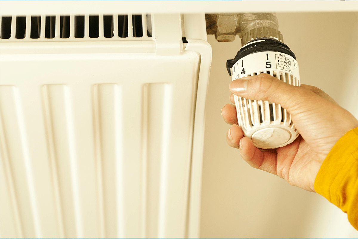 Eine Person dreht am Heizkörper-Thermostat.