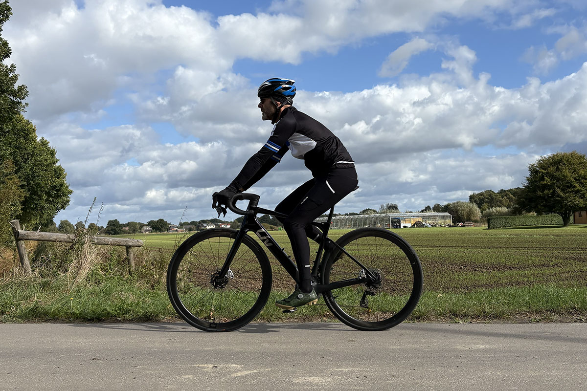 Mann fährt auf E-Rennrad auf einer Straße, die an einem Feld vorbei führt.