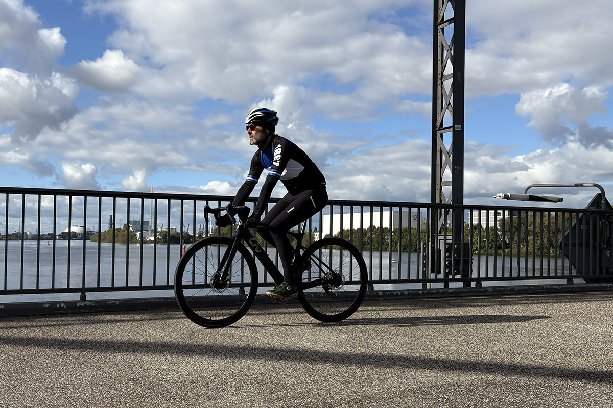 Mann fährt auf E-Rennrad über eine Brücke, die über einen Fluss verläuft.