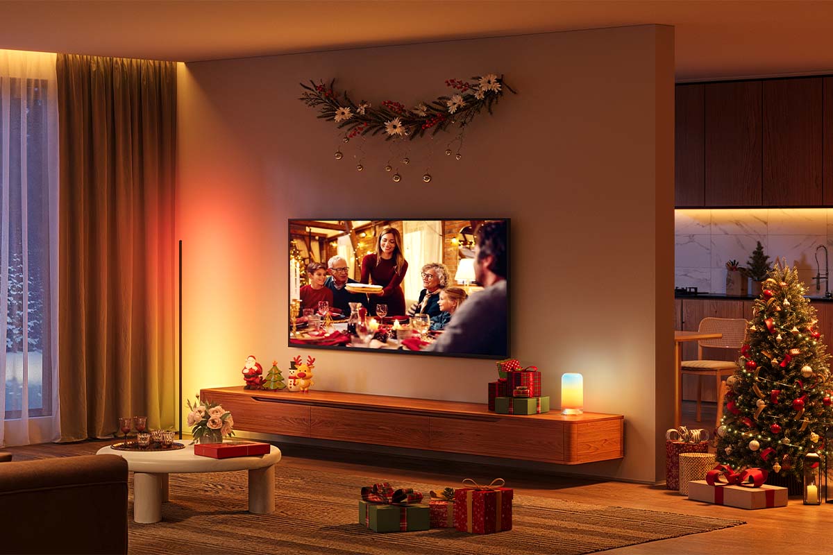 Stimmungsvoll beleuchtetes Wohnzimmer, man sieht einen Fernseher, daneben einen geschmückten Weihnachtsbaum