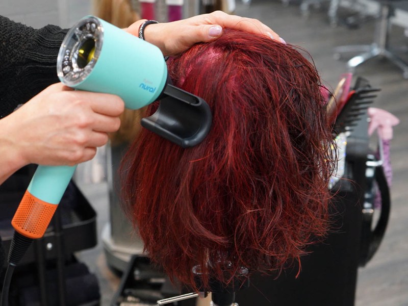 Eine Person föhnt einen lebensgroßen Puppenkopf mit dem Dyson Supersonic Nural und Aufsatz gegen Frizz.