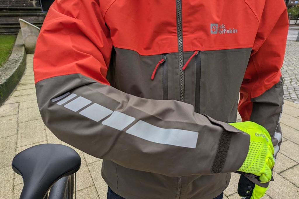 Detailaufnahme einer Regenjacke, die von einer Person getragen wird. Man sieht einen Ärmel mit reflektierenden Elementen