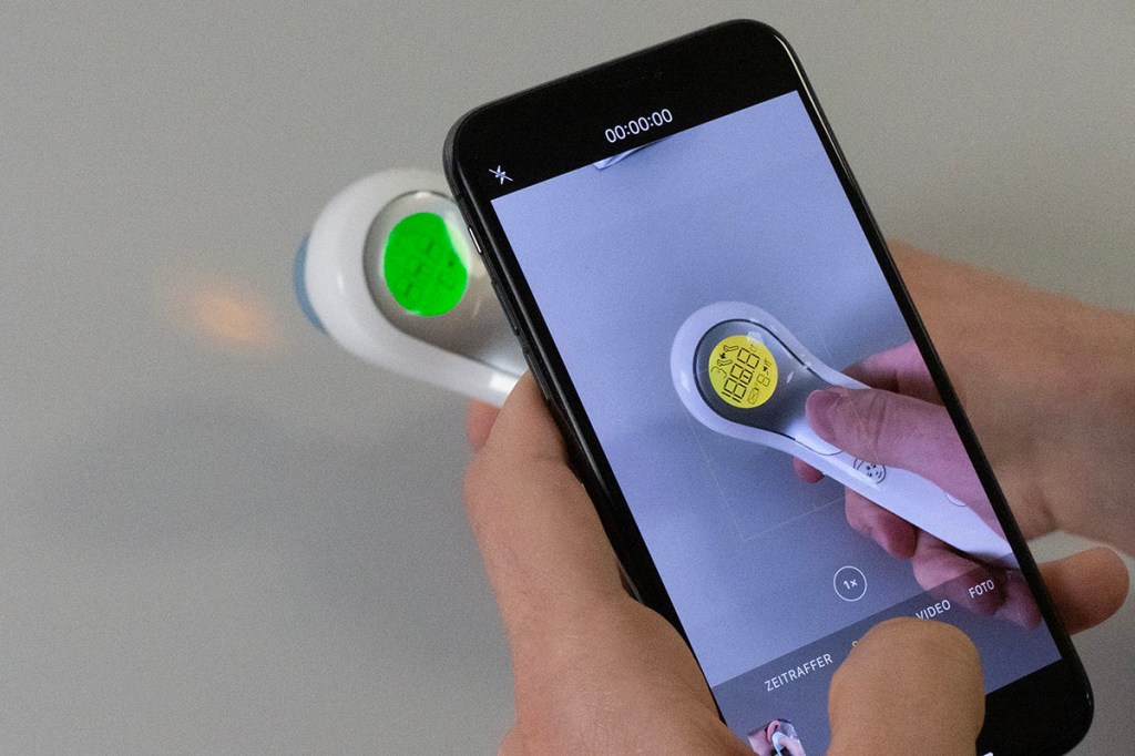 Durch Smartphone-Display betrachtetes kontaktloses Fieberthermometer.